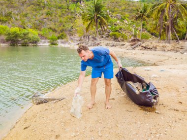 Eldivenli adam denizi kirleten plastik torbalar alıyor. İnsan yapımı kirlilik ve çevresel kirliliğin yol açtığı kumsala çöp dökme sorunu, konsept olarak gönüllü temizleme kampanyası