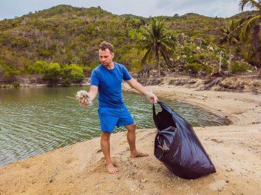 Eldivenli adam denizi kirleten plastik torbalar alıyor. İnsan yapımı kirlilik ve çevresel kirliliğin yol açtığı kumsala çöp dökme sorunu, konsept olarak gönüllü temizleme kampanyası