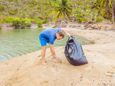Eldivenli adam denizi kirleten plastik torbalar alıyor. İnsan yapımı kirlilik ve çevresel kirliliğin yol açtığı kumsala çöp dökme sorunu, konsept olarak gönüllü temizleme kampanyası