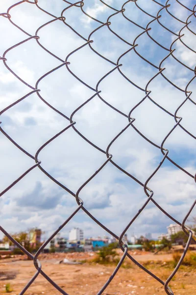 Close-up old iron wire fence vintage net on the background of city view with blue cloudy sky. Vertical format