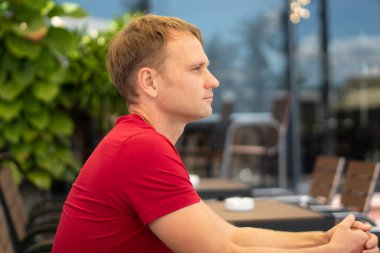 Yarım portre, kısıtlı gülümseme, gündelik kırmızı tişörtlü yakışıklı genç adam modern kafede oturuyor, mutlu bakışlar, birini bekliyor ya da çoktan tanışmış. İnsan ilişkisi, iyi gelecek kavramı değiştirir.