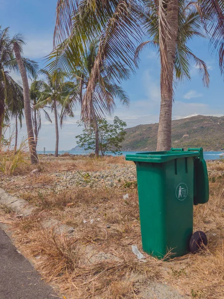 Membuka tempat sampah plastik hijau kosong di desa modern yang nyaman dekat laut dan telapak tangan. Pengendalian infeksi, pembuangan sampah, pembuangan konsep limbah. Format vertikal cerita — Stok Foto