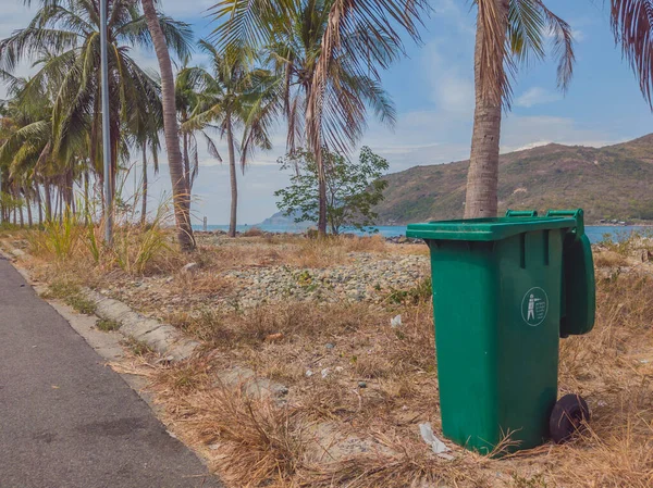 Membuka tempat sampah plastik hijau kosong di desa modern yang nyaman dekat laut dan telapak tangan. Sampah umum di pinggir jalan. Pengendalian infeksi, pembuangan sampah, pembuangan konsep limbah — Stok Foto