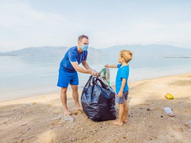 Genç mutlu aile eylemcileri plajda plastik atık topluyor. Baba ve oğul gönüllü olarak çöpleri temizliyor. Çevre kirliliği sorunları. Açık hava yaşam tarzı eğlencesi. Çocukların doğal eğitimi