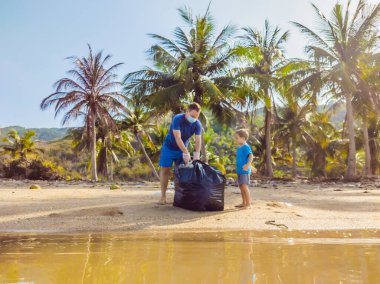 Genç mutlu aile eylemcileri plajda plastik atık topluyor. Baba ve oğul gönüllü olarak çöpleri temizliyor. Çevre kirliliği sorunları. Açık hava yaşam tarzı eğlencesi. Çocukların doğal eğitimi