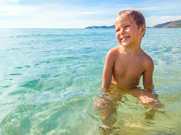 Європейський хлопчик плаває і грає в блакитній прозорій морській воді азура. Він відпочиває під час літніх канікул. Подорож і щастя, ідея щасливого дитинства — стокове фото
