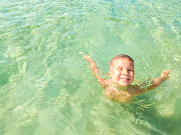 Europese jongen zwemt en speelt in blauw helder azur zeewater. Hij ontspant zich tijdens zijn zomervakantie. Reizen en geluk, gelukkige kindertijd concept — Stockfoto