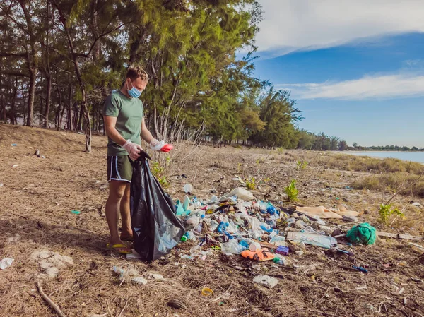Man in gloves pick up plastic that pollute sea and forest. Problem of spilled rubbish trash garbage on the beach sand caused by man-made pollution, campaign to clean volunteer in concept