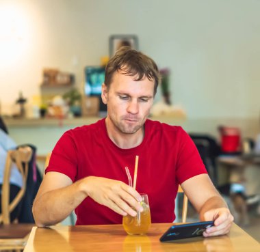 Düşünceli, düşünceli, düşünceli, düşünceli genç adam kafeteryada Chia ice tea içerek akıllı telefonla mesaj gönderiyor. Gerçek insanlar ifade eder, hayat sorunları çözer ve iletişim kurar