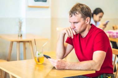 Düşünceli, düşünceli, düşünceli, düşünceli genç adam kafeteryada Chia ice tea içerek akıllı telefonla mesaj gönderiyor. Gerçek insanlar ifade eder, hayat sorunları çözer ve iletişim kurar