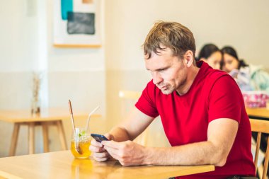 Düşünceli, düşünceli, düşünceli, düşünceli genç adam kafeteryada Chia ice tea içerek akıllı telefonla mesaj gönderiyor. Gerçek insanlar ifade eder, hayat sorunları çözer ve iletişim kurar