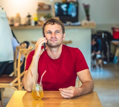 Kısıtlanmış gülümseme mutlu genç adam kafede kırmızı gömlekli akıllı telefona cevap verir, buzlu çay içer, birini bekler ya da iş birliği yapar. Gerçek insanlar ifade eder, hayat sorunları çözer, iletişim kurar, ilişki kurar