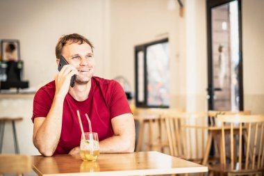 Gülümse mutlu genç adam kafede kırmızı gömlekli akıllı telefona cevap ver, buzlu çay iç, birini bekle ya da iş birliği yap. Gerçek insanlar ifade eder, hayat sorunları çözer, iletişim kurar, ilişki kurar