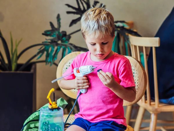Boy menggunakan pistol lem cair panas membuat sendiri mainan DIY dari bahan cangkir plastik daur ulang. Mendukung kreativitas kerajinan tangan, rekreasi kreatif untuk pendidikan anak-anak di dalam ruangan atau sekolah rumah karantina — Stok Foto