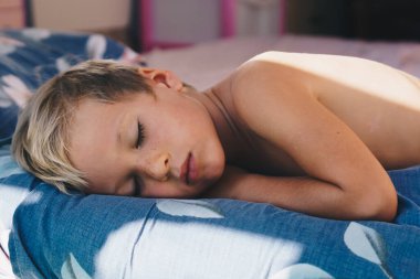 Cute little boy sleep sweetly on pillow with bright morning sunbeams from window, taking a nap. Happy bedtime for kids. Problem of early awakening, late falling asleep, health sleep biorhythms clipart