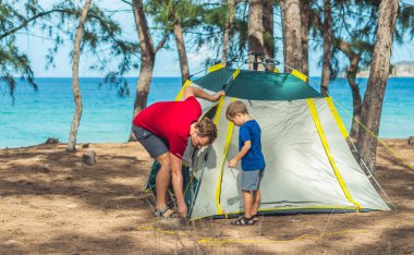 Kamp yapan turistler, yaz ormanlarında Lazur Denizi yakınlarında yeşil gri kamp alanlarını kuruyorlar. Tatlı çocuk babasının çadır kurmasına yardım ediyor. Çocukların doğal eğitimi