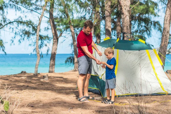 Camping orang asing gaya hidup wisatawan memasang mendirikan berkemah hijau abu-abu mereka di hutan musim panas dekat laut lazur. Anak laki-laki yang lucu membantu ayahnya merakit tenda. Pendidikan alami anak-anak — Stok Foto