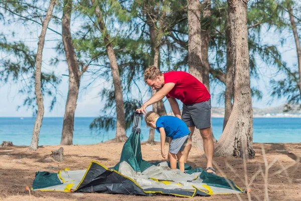 Menempati orang-orang dengan gaya hidup luar ruangan, para wisatawan mendirikan perkemahan abu-abu hijau di hutan musim panas dekat laut lazur. Anak laki-laki membantu ayah mempelajari mekanisme modern mudah untuk melipat tenda. Pendidikan anak alami — Stok Foto