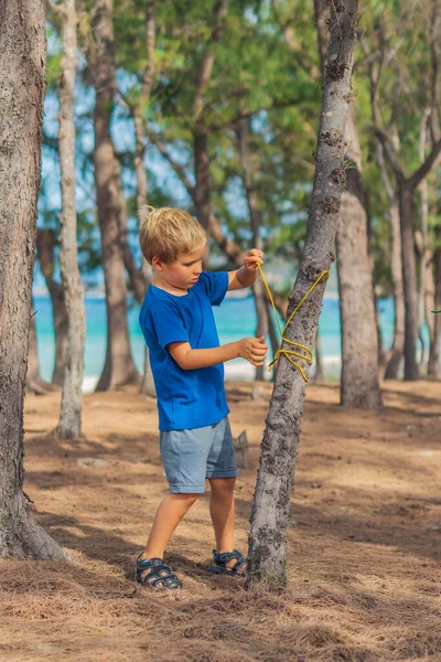 Camping orang asing gaya hidup wisatawan di hutan musim panas dekat laut lazur. Anak laki-laki gemuk serius dalam biru t-shirt belajar teknik bertahan hidup, metode praktek mengikat tali knot. Pendidikan anak alami — Stok Foto