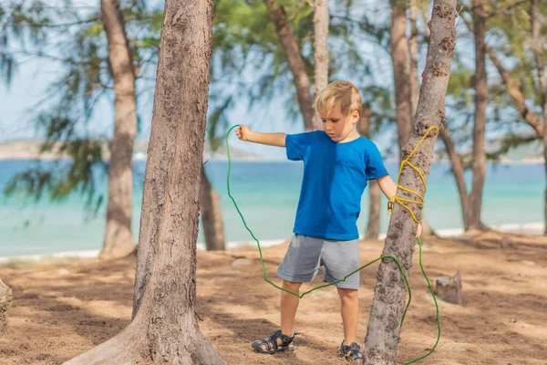Teltturister utendørs i sommerskog ved Lazur-sjøen. Blond, seriøs gutt i blå t-skjorte, overlevelsesteknikker, metoder for å knyte tauknuter. Naturbarnsundervisning – stockfoto