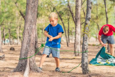 Kamp insanları Lazur Denizi yakınlarındaki yaz ormanlarında yaşam tarzı turistleri. Mavi tişörtlü sarışın ciddi çocuk hayatta kalma teknikleri öğreniyor, ip düğüm atma yöntemleri uyguluyor. Doğal çocuk eğitimi