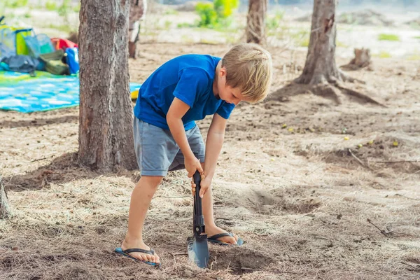 Camping människor utomhus livsstil turister, sommar skog nära lazur havet. Blond pojke leker studera överlevnadstekniker, öva metoder för att gräva jorden med en spade. Naturlig utbildning för barn — Stockfoto