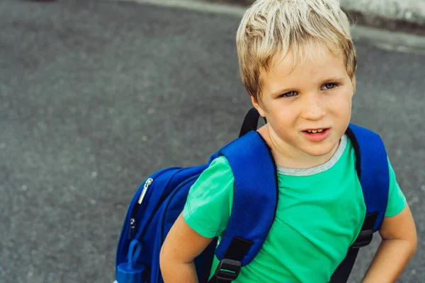 Lustige verschmitzte süße blonde Junge mit Sommersprossen blauen Rucksack aus der Schule oder dem Kindergarten, künstlerische Emotionen Gesichtsausdruck. Mikromomente einfache Freuden glückliche Kindheit, Bildungsprobleme Psychologie — Stockfoto