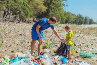 Mavi maskeli gönüllüler. Baba, oğul Lazur Denizi yakınlarındaki kumsalı kirleten çöpleri toplayın. Dökülen çöplük gezegeni kirliliği çevresel koruma sorunu. Doğal çocuk eğitimi