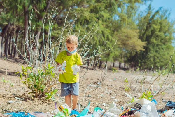 Volunteer boy in face mask helps to pick up garbage which pollute beach near forest. Problem of spilled rubbish trash planet pollution environmental protection concept. Natural children education