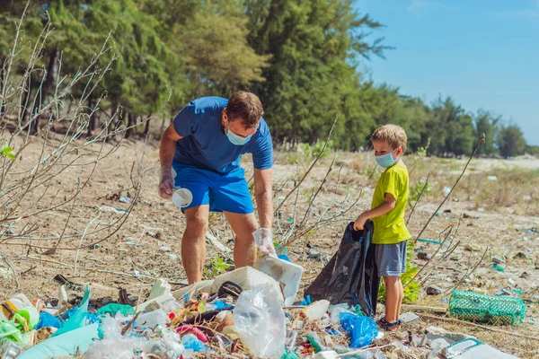 Volunteers in blue face mask. Father, son pick up garbage which pollute beach near lazur sea. Problem of spilled rubbish trash planet pollution environmental protection. Natural children education