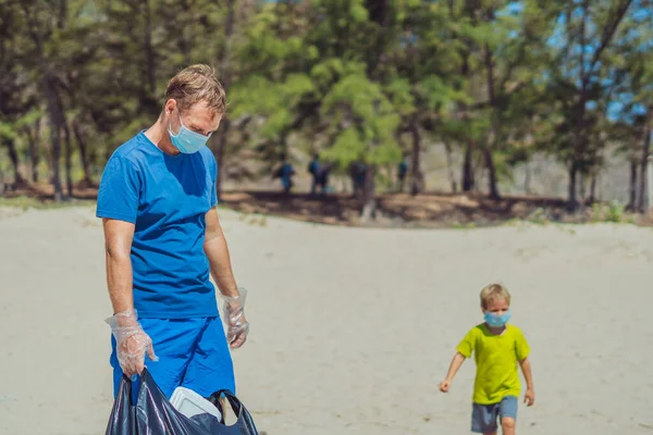 Volunteer wajah biru masker hutan pasir pantai. Ayah menunggu anak aktif membantu mengambil sampah ke dalam tas hitam. Masalah tumpah sampah sampah planet polusi perlindungan lingkungan. Pendidikan anak alami — Stok Foto