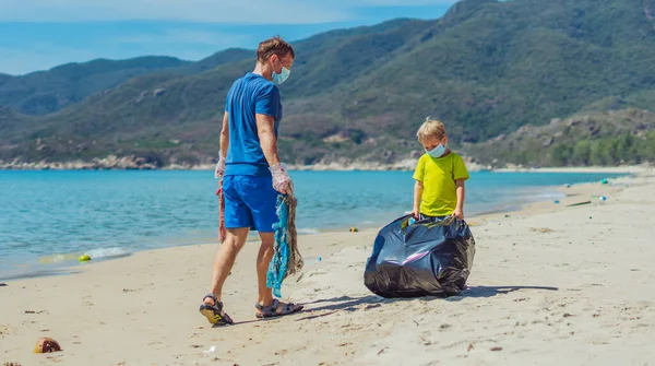 Topeng wajah biru volunteer lazur pantai pasir laut. Anak membantu ayah memegang tas hitam untuk mengambil sampah. Masalah tumpah sampah sampah planet polusi perlindungan lingkungan. Pendidikan anak alami — Stok Foto