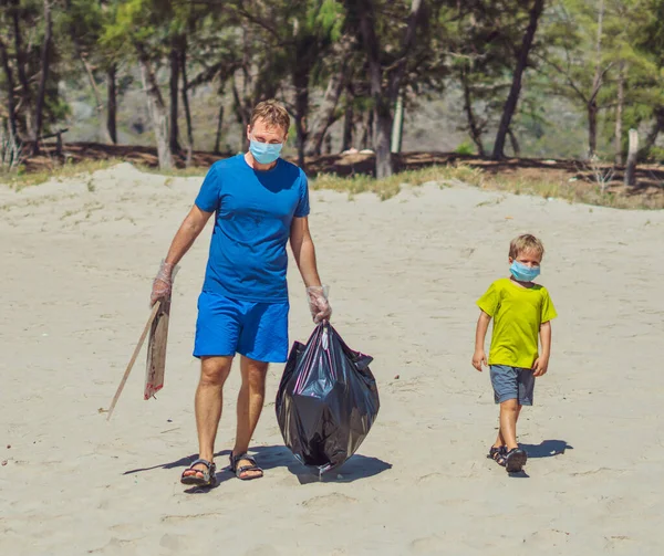 Volunteer wajah biru masker hutan pasir pantai. Anak pergi, ayah memegang tas hitam dengan mengambil sampah. Masalah tumpah sampah sampah planet polusi perlindungan lingkungan. Pendidikan anak alami — Stok Foto
