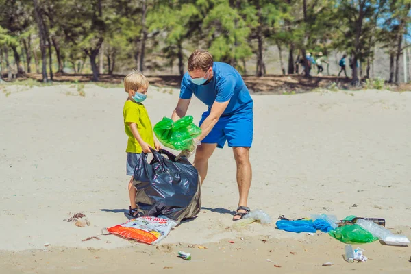 Volunteer blue face mask forest sand beach. Son helps father hold black bag for pick up garbage. Problem spilled rubbish trash planet pollution environmental protection. Natural children education