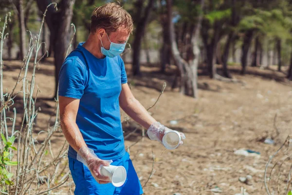 Sukarelawan bertopeng biru Hutan pasir pantai. Pria aktif mengambil sampah plastik tas peralatan makan sekali pakai. Sampah tumpah sampah planet polusi perlindungan lingkungan. Masalah sosial alami — Stok Foto