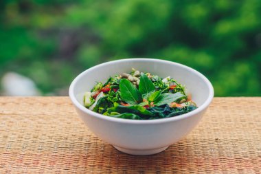 Yeşil yapraklardan güzel çiğ vegan salatası beyaz tabakta sebzeleri karıştırır. Pişirme tarifi. Domates, havuç, karnabahar maydanoz, salatalık, fesleğen, balkabağı tohumu, yosun.