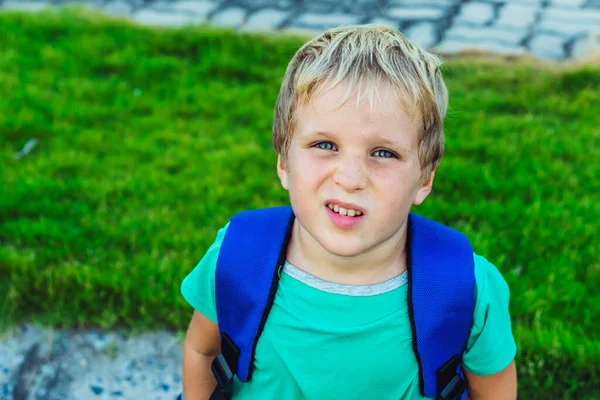 Handsome cute blond boy green t-shirt blue backpack in bad mood look camera. Emosi artistik dan gerak tubuh. Masalah atau bahagia masa kecil, perilaku psikologi pendidikan, konsep hubungan keluarga — Stok Foto