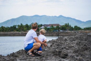 Baba çömelmiş, kucaklaşan oğul, göl kenarında el ele tutuşup uzaklara bakıyor. Mutlu çocukluk, babalık. Aile birlikte yürür. Evde doğal eğitim, babaların günlük sorumlulukları etkili.