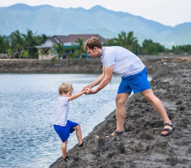 Dad helps son go down to lake water, explains safety rules. Family together walk play. Home natural child education, fathers day, fatherly responsibilities, influence on formation of son worldview clipart