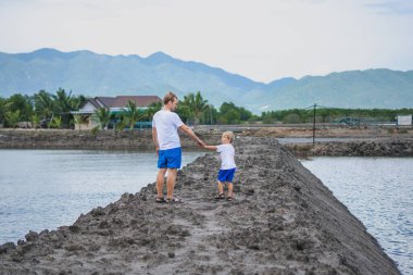 Baba oğul dağ gölünün yanında yürüyor, göz kırparken birbirinize bakın. Mutlu bir çocukluk. Evde doğal çocuk eğitimi, babalar günü, baba sorumlulukları, oğul dünya görüşü düzeni üzerindeki etkisi.