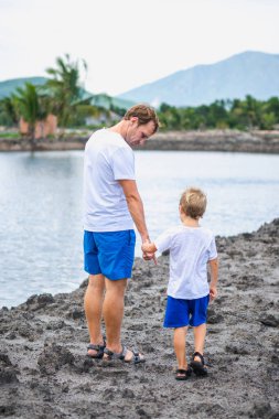 Baba, göl kenarında yürürken oğluna göz kulak ol. Mutlu bir çocukluk. Evde doğal eğitim, babalar günü, baba sorumlulukları, oğul dünya görüşü oluşumu üzerindeki etkisi