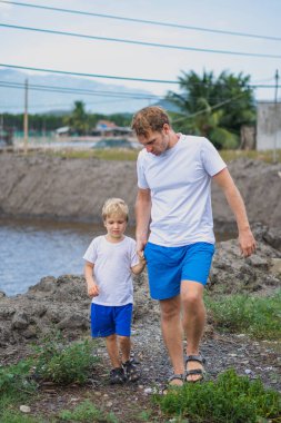 Baba, göl kenarında yürürken oğluna göz kulak ol. Mutlu bir çocukluk. Evde doğal eğitim, babalar günü, baba sorumlulukları, oğul dünya görüşü oluşumu üzerindeki etkisi