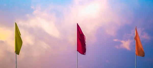 Varování nebo znamení pozornosti, gratuluji podepsat tři červené žluté oranžové vlajky na pozadí barvy večera jasně dramatické růžová obloha západ slunce cloudscape panorama. Ideální pro design tapety — Stock fotografie