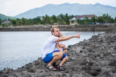 Baba çömelmiş, sarılmış oğul, uzaklara bakıyor. Mutlu çocukluk, babalık. Aile birlikte yürür. Evde doğal eğitim, babaların günlük sorumlulukları oğul dünya görüşünün oluşumunu etkiler.
