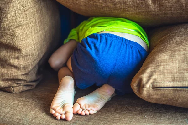 Rear view, back butt legs feet of a child hiding under a pillow, offended boy in bad mood or playing. Funny photo. Family relationship, childhood problems and behaviour concept, education psychology — Stock fotografie