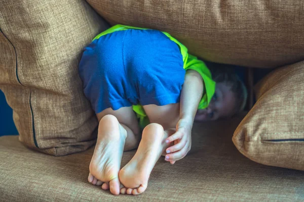 Rear view, back butt legs feet of a child hiding under a pillow, offended boy in bad mood or playing. Funny photo. Family relationship, childhood problems and behaviour concept, education psychology — kuvapankkivalokuva