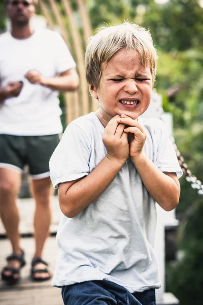 Menino chorão tocando a mandíbula da boca do queixo, olhos fechados, rugas se contorcendo por causa da dor. Conceito de assistência médica primeiros socorros enquanto caminham no parque — Fotografia de Stock