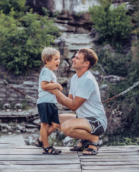 Father hugs tickle son sitting squatting, smile. Happy childhood, fathers day, mountain, chain background as symbol of strong bond between dad and child. Father influence on son worldview — Stock Photo, Image