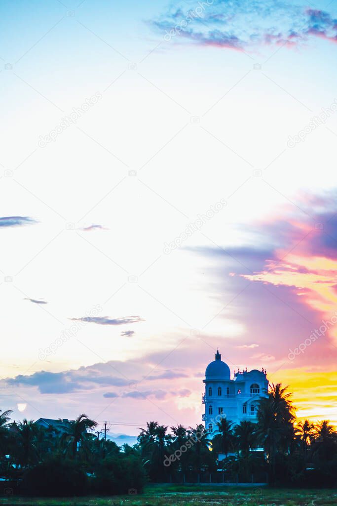 Dark orange red yellow purple colorful natural bright sunset sky. Evening cloudscape reflected in water, background building in shadow, ducks floating in rice field. Design wallpaper