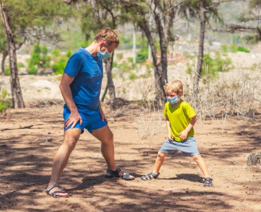 Spor baba oğul ormanda temiz hava alıyor, birlikte antrenman yapıyor, çömelme ve yan bükme tekniği uyguluyor, maske takıyor, Coronavirus yürüyüş doğa güneşini koruyor. Baba oğlanı etkiler.